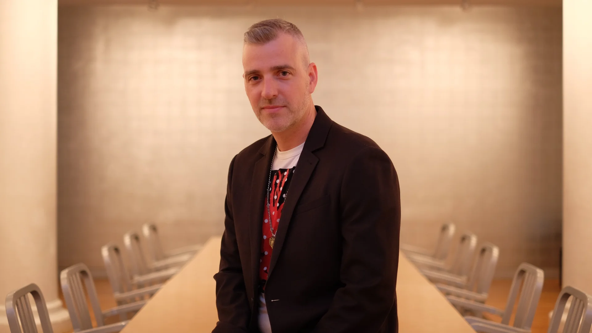 A white man on a suit sitting on a table in a board room
