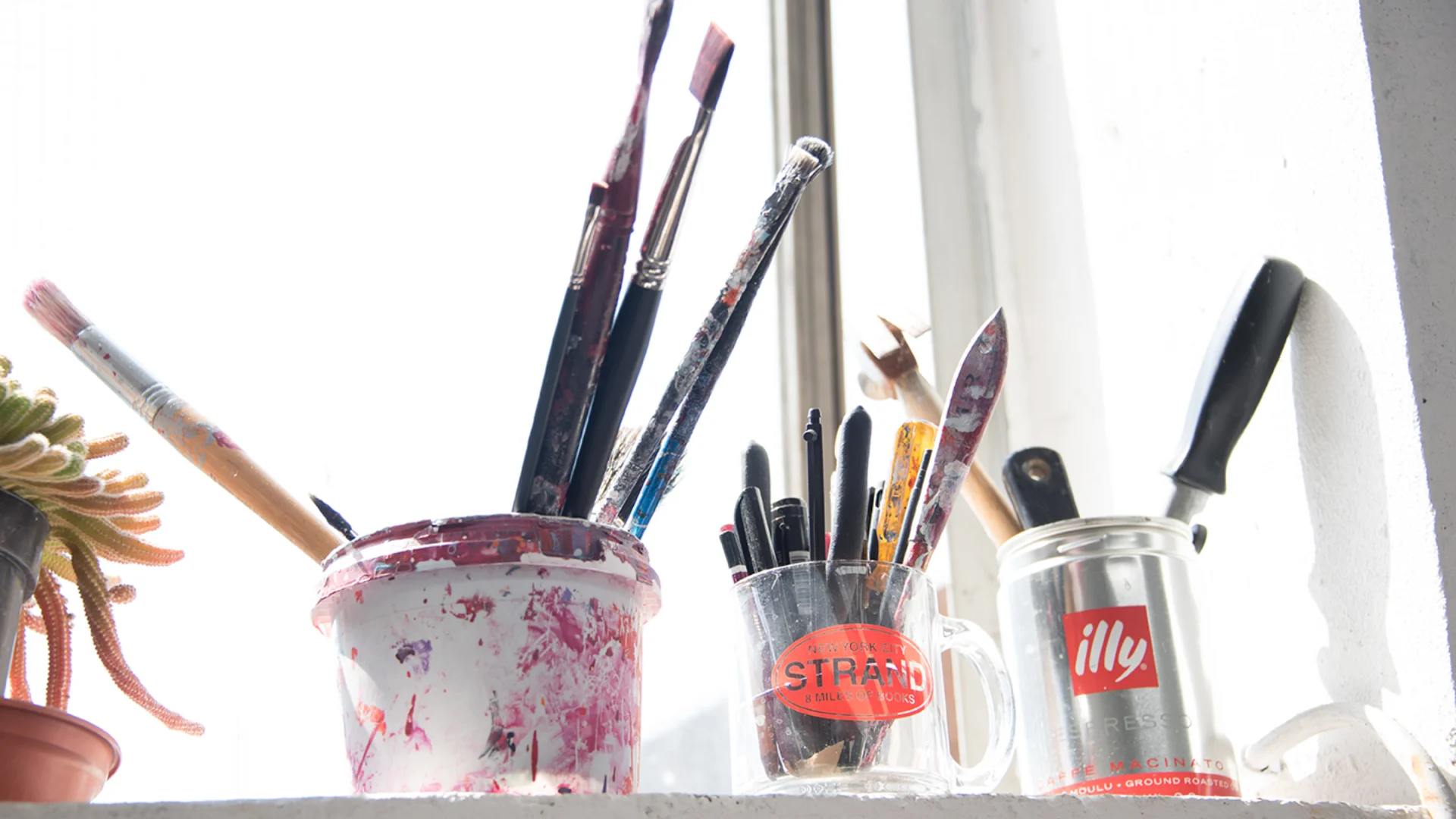 Paints and tools in plastic pots on window sill