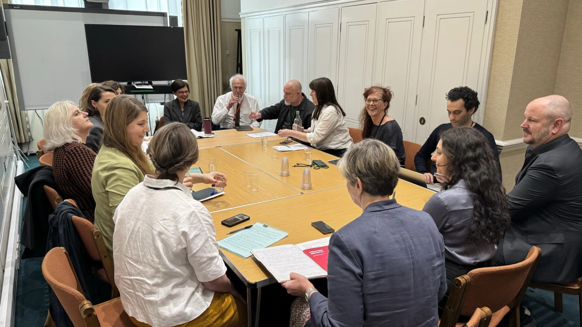A number of people around a table discussing in a white room.