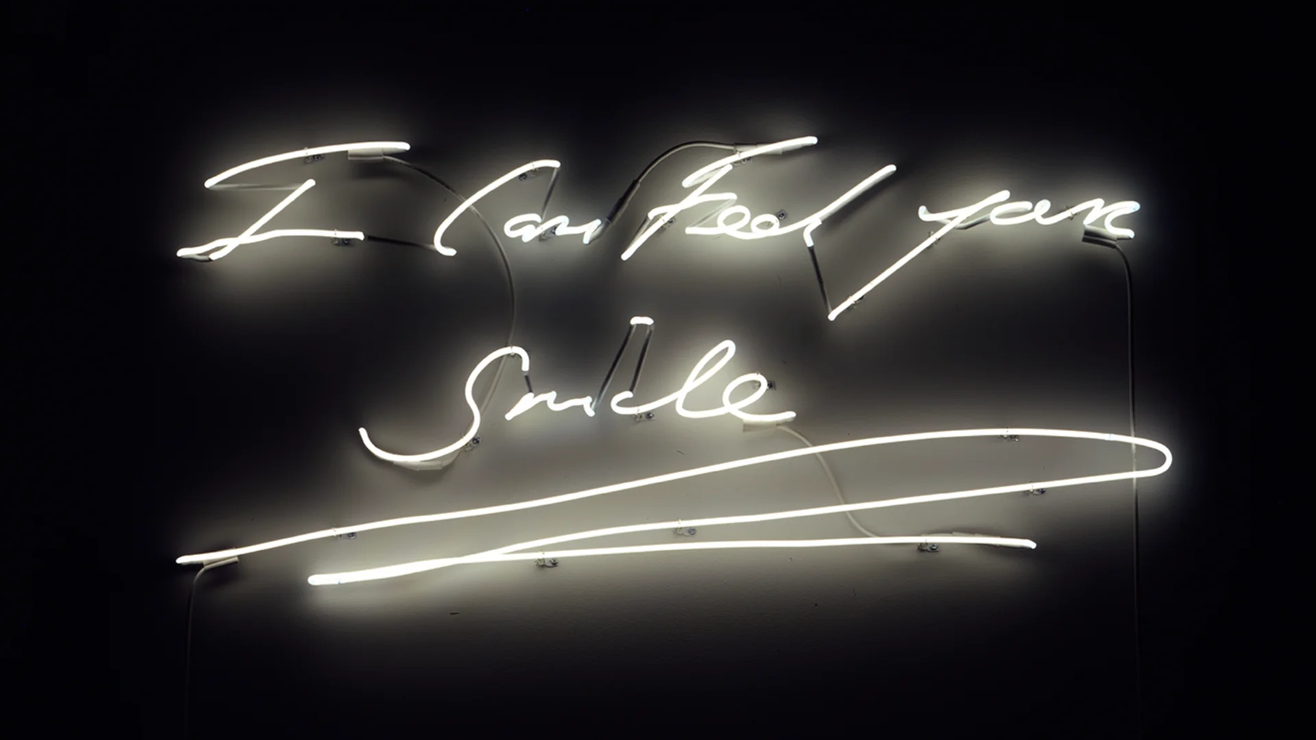 White neon lights on a black background saying 'I can feel your smile'.