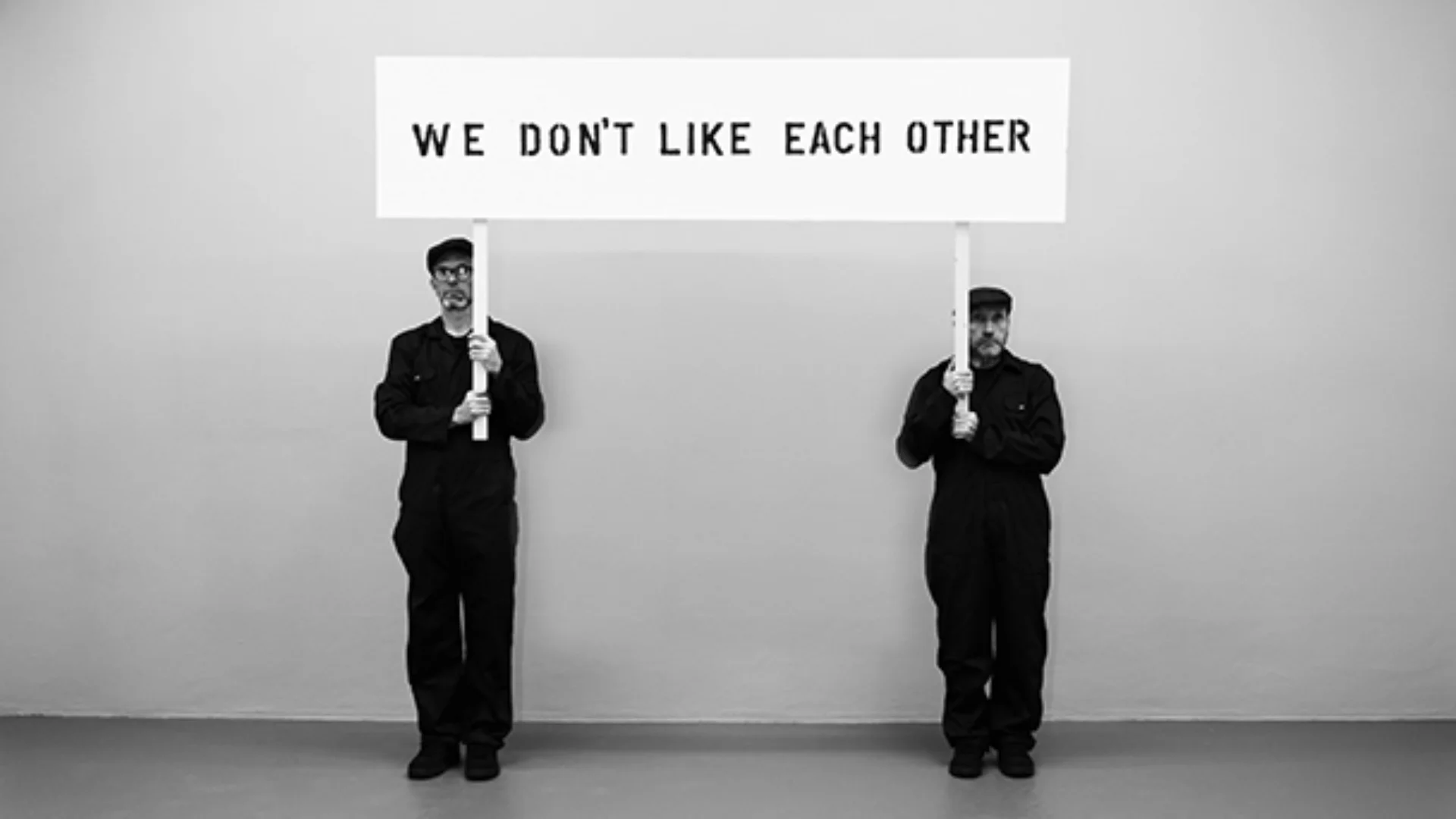 Demo Tape - still from video 'Demo Tape’ (2020) two men hold sign saying We Don't Like Each Other.