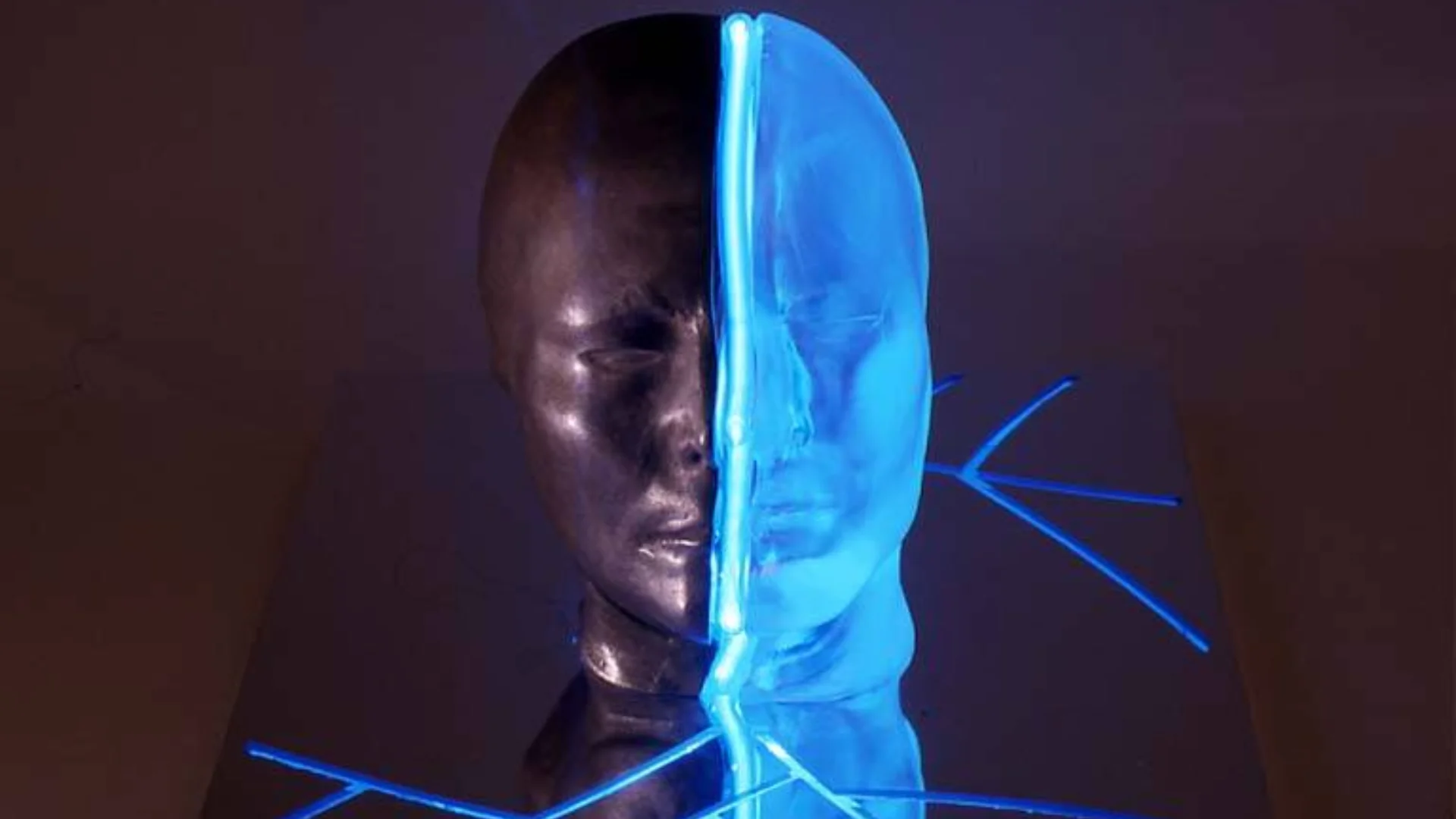 Photo of a face in two sections - the left half is a dark stature and the right is a translucent blue and illuminated