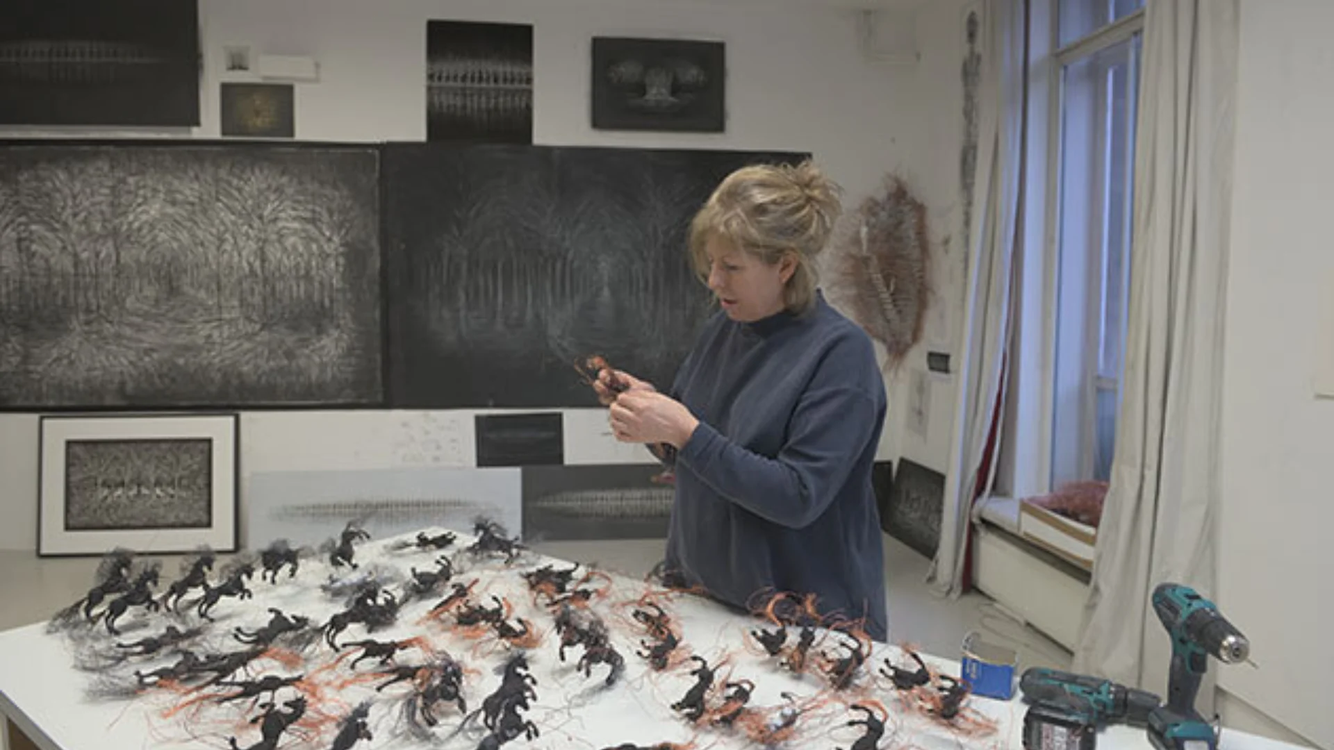 Artist preparing exhibition. Many small horse models being attached to a white board