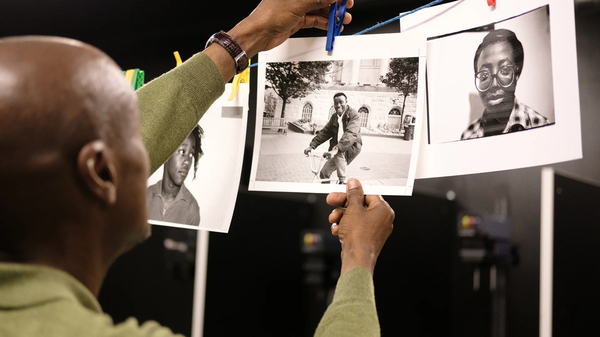 A close-up of a black man clipping freshly developed photographs in a studio