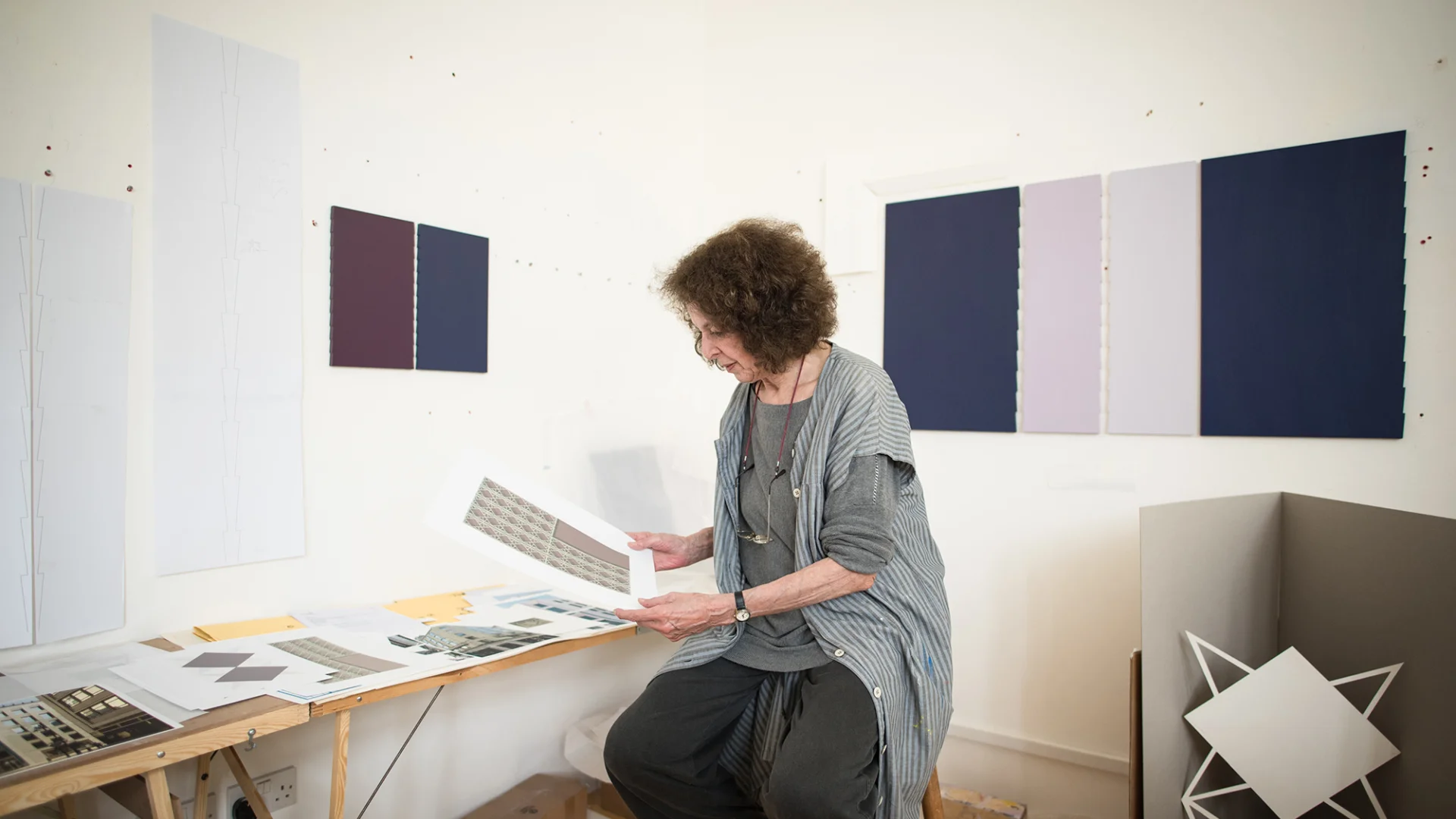 A white woman sitting, looking at her prints in her studio