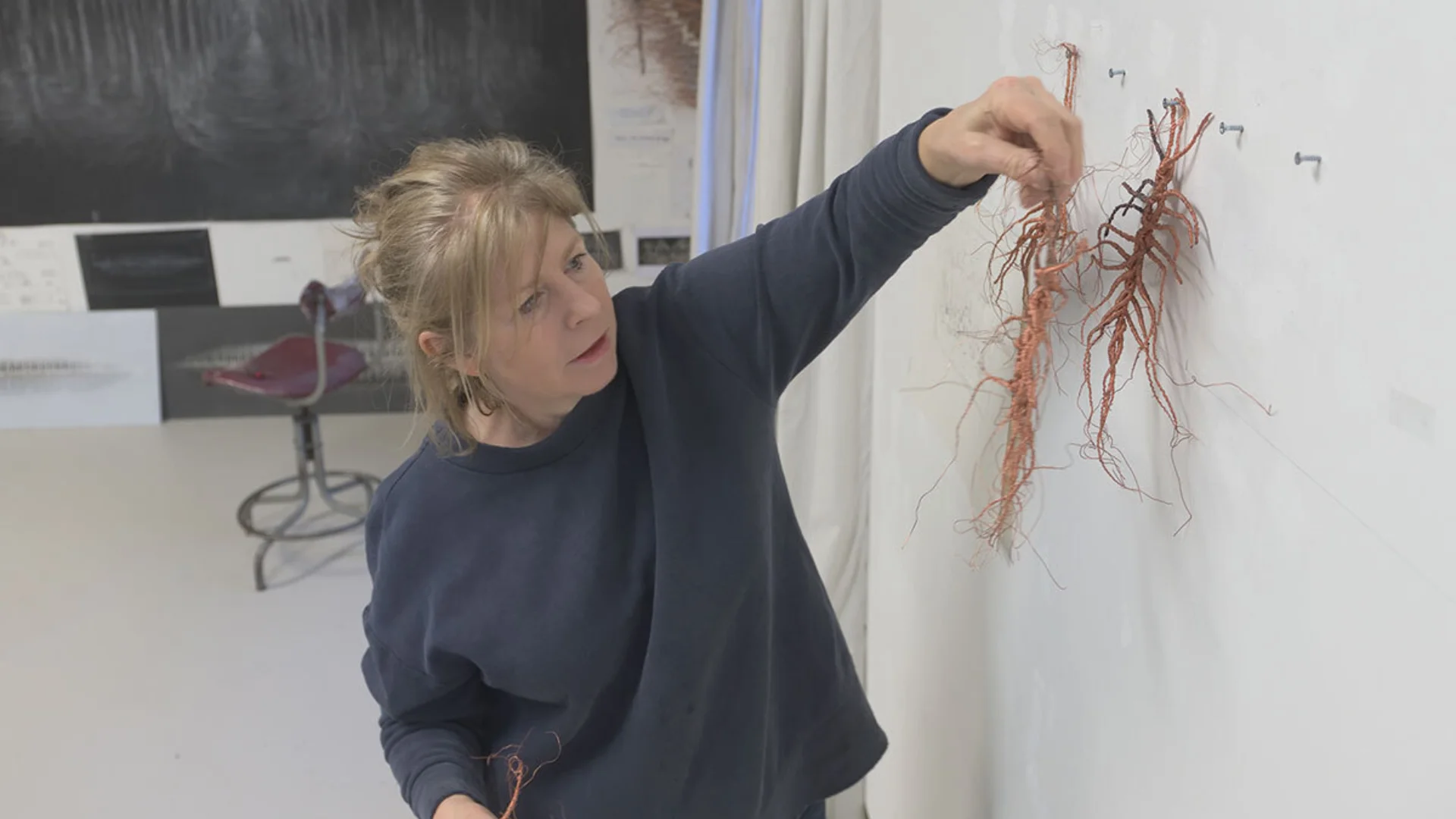 A white woman hanging a small artwork on a white wall, perspective from above.