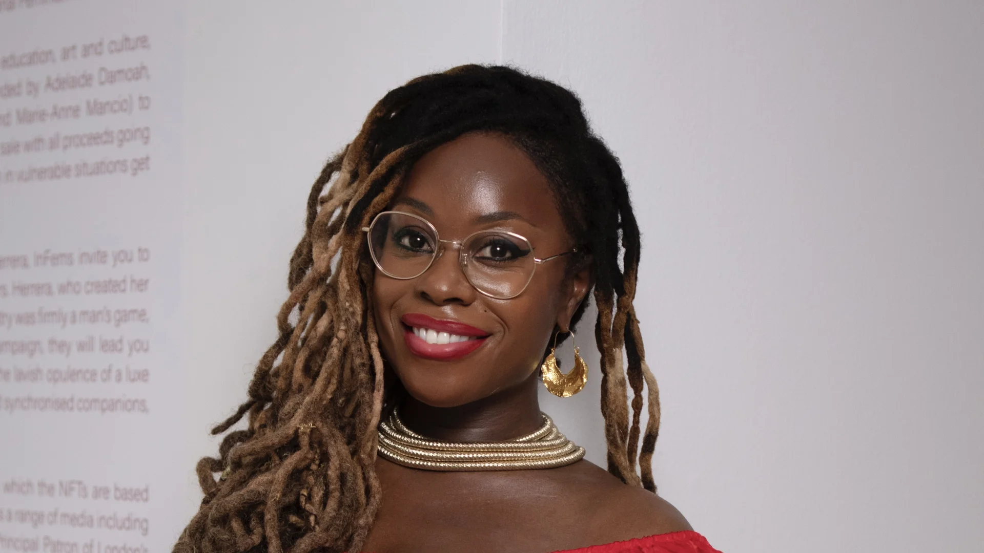 A black woman with glasses and braids, wearing a red dress