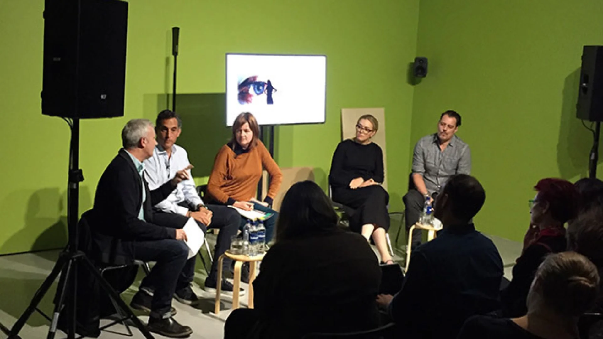 A panel of five people sitting in front of a green screen