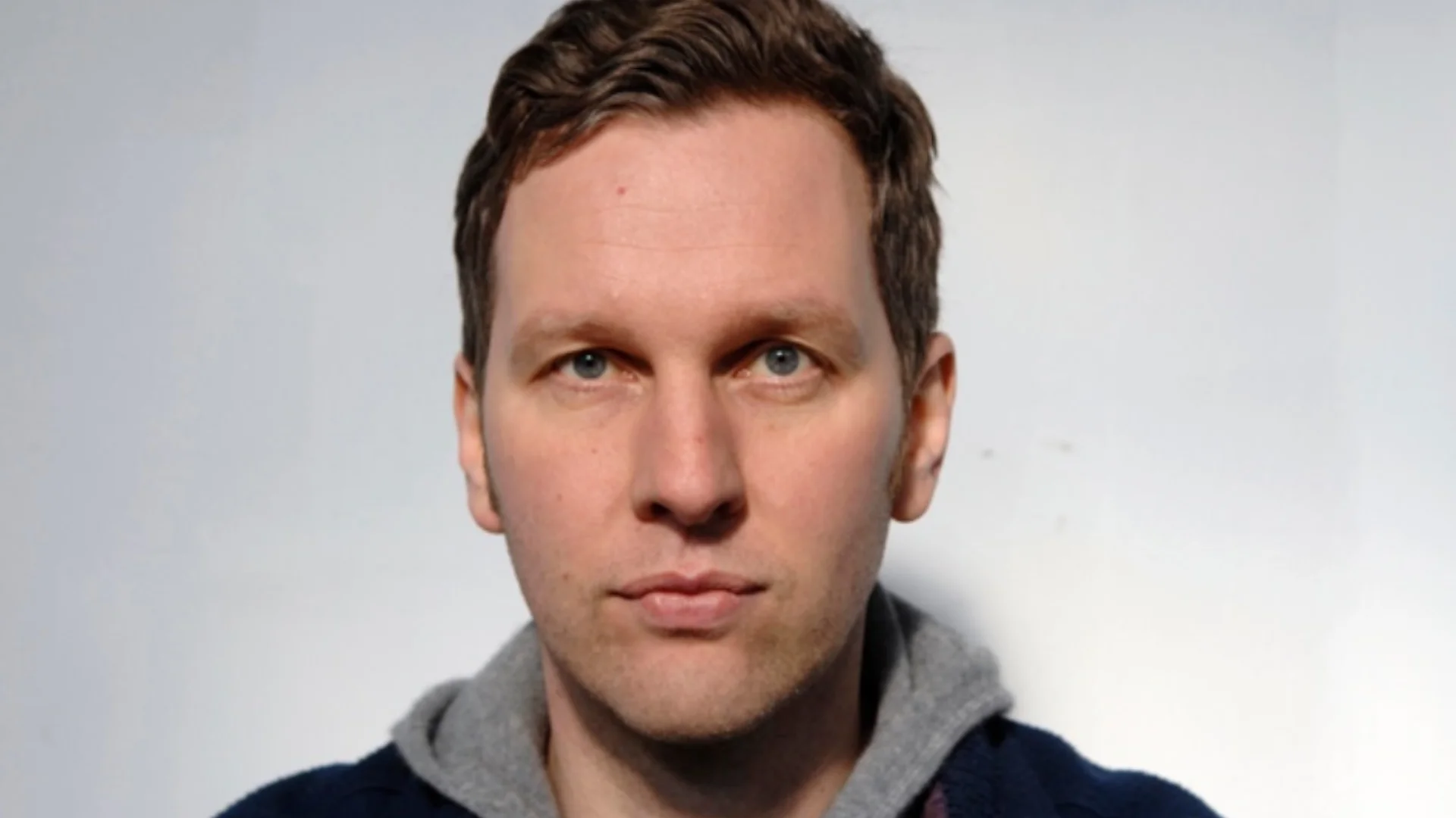 A close-up portrait of a white man with sort blonde hair looking at the camera