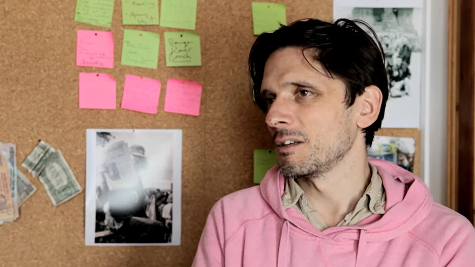 A white man with short black hair and a pink jumper talking to the camera