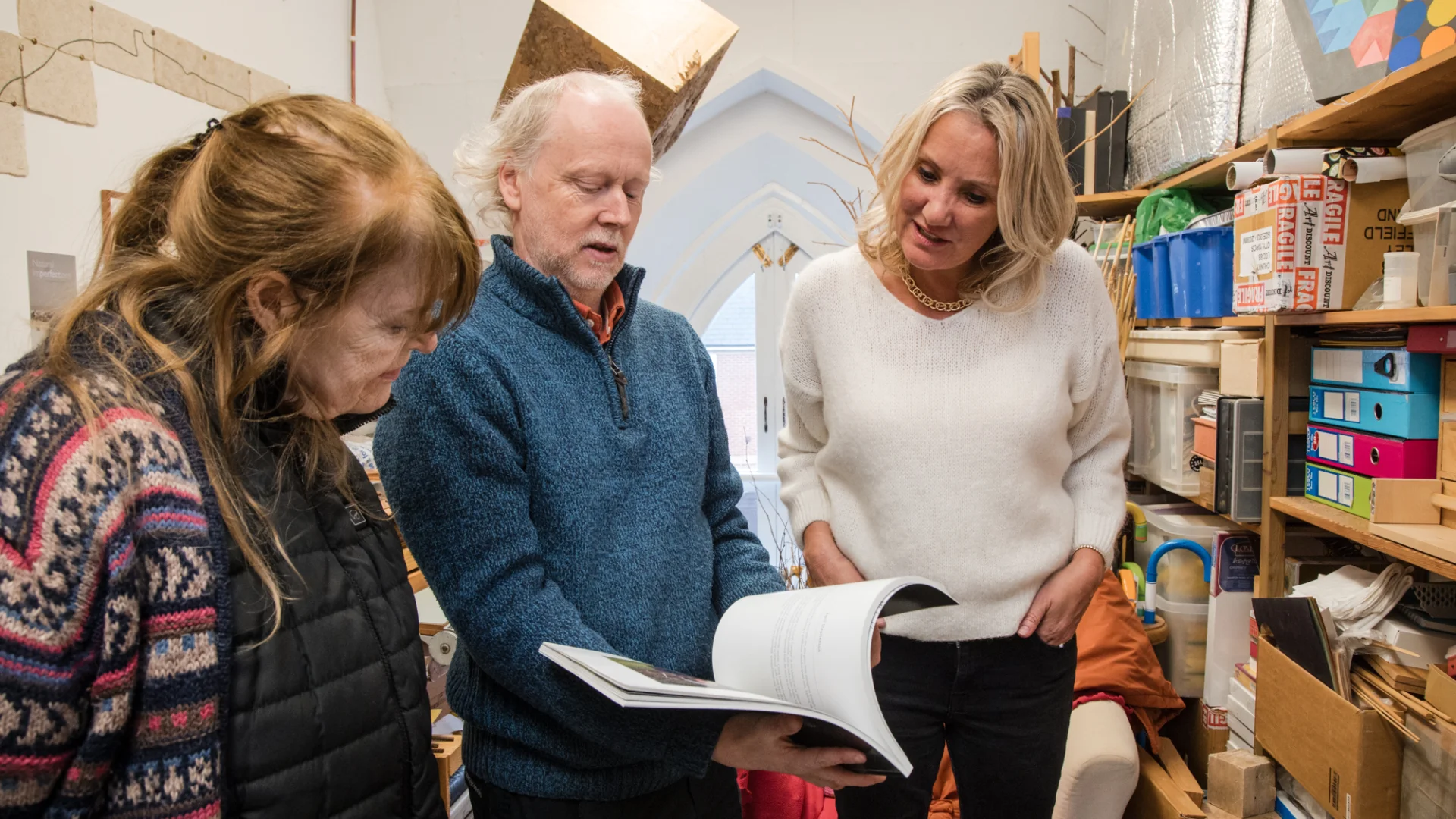 three people looking at an artists' book. The person in the middle is holding the book open.