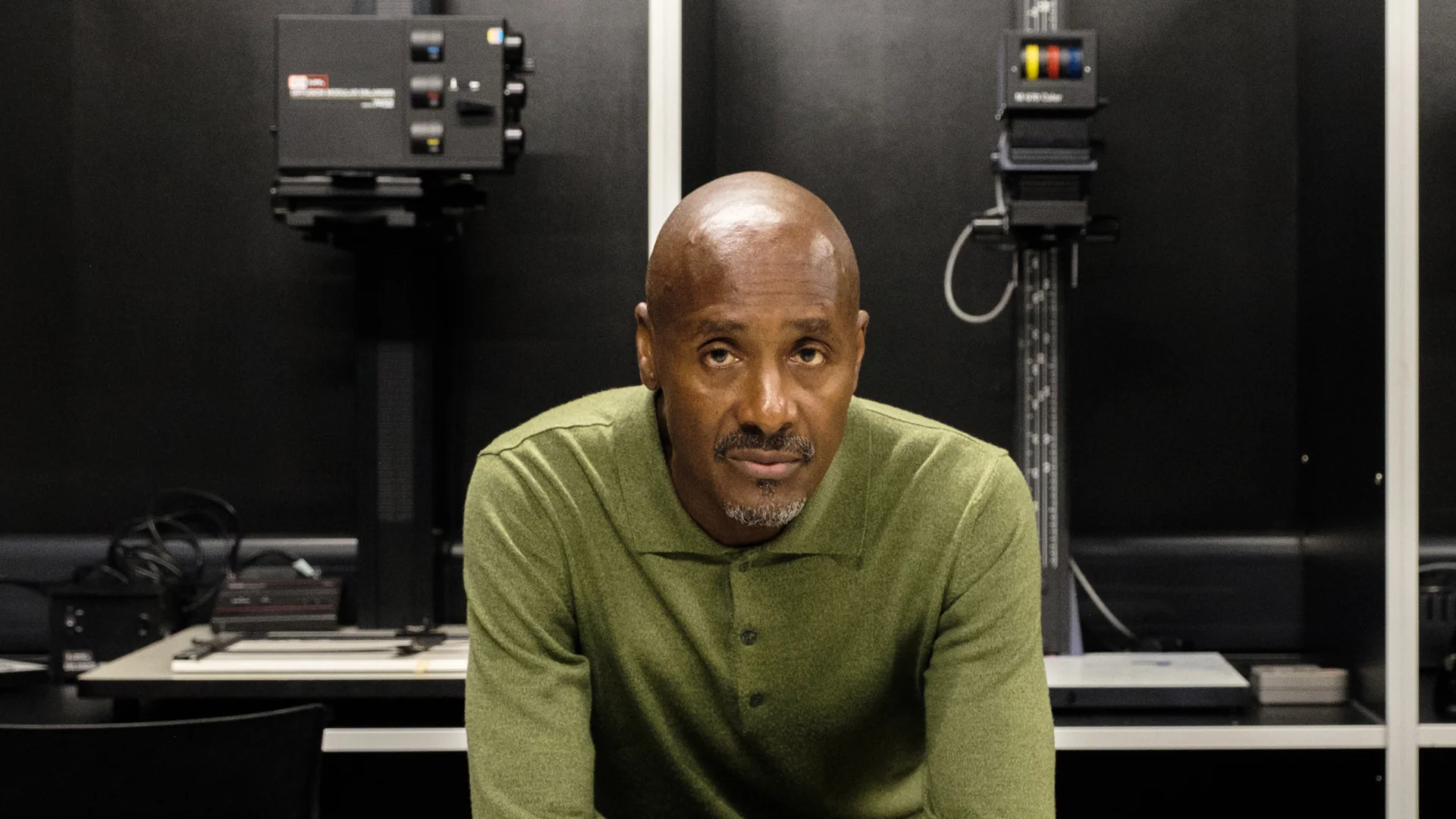 A black man standing above some black and white printed photography.
